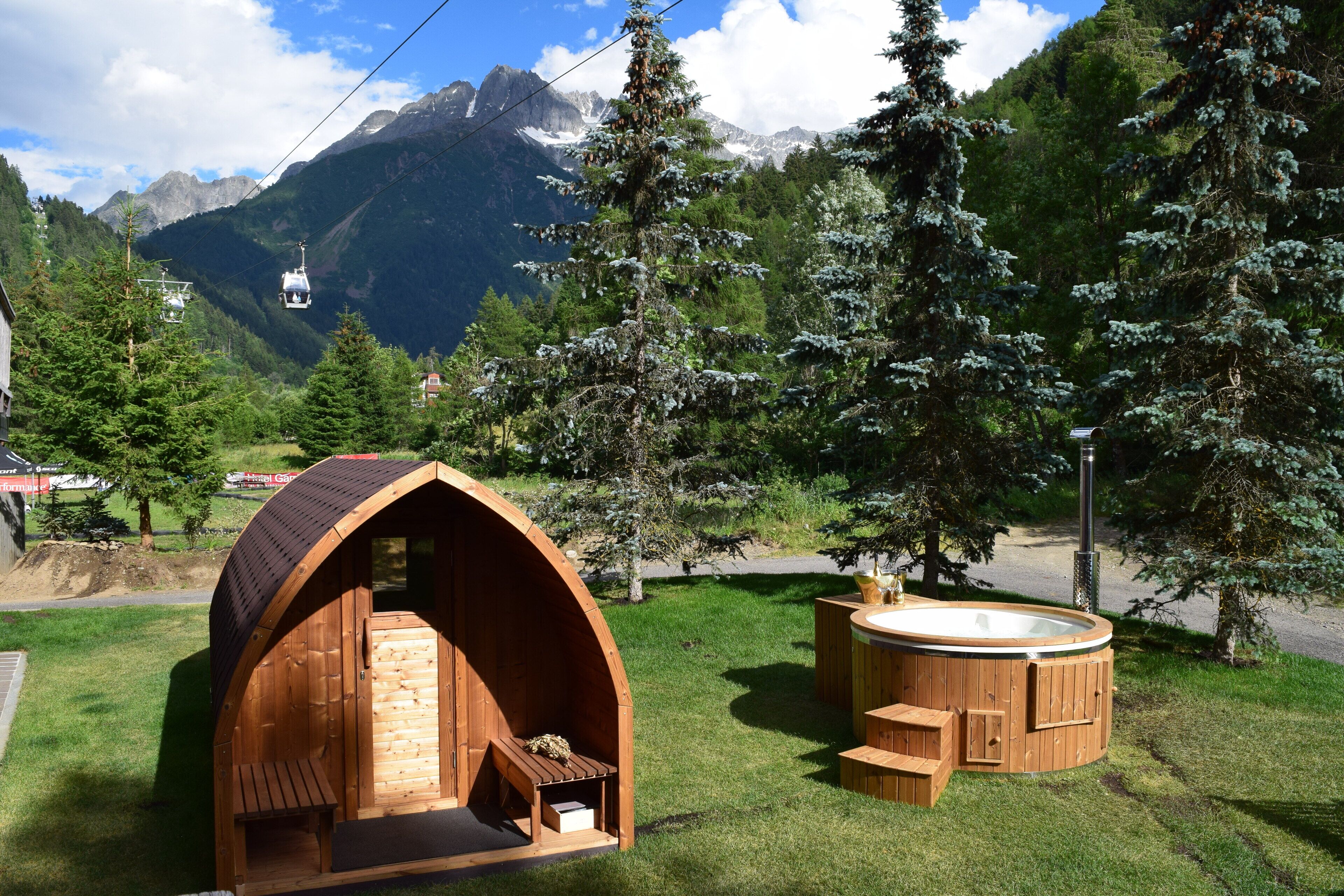 Una cabaña de madera con jacuzzi y banco, rodeada de árboles y montañas.
