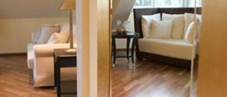A room with a wooden floor, a sofa, a small table, and a lamp.