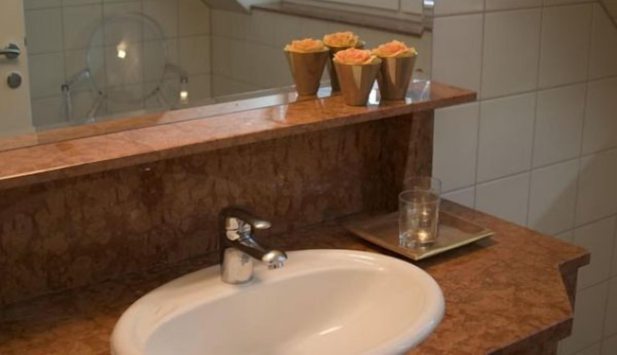 Une salle de bain avec un lavabo en marbre, un miroir et une étagère sur laquelle sont posés trois objets de couleur orange.