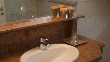 Une salle de bain avec un lavabo en marbre, un miroir et une étagère sur laquelle sont posés trois objets de couleur orange.