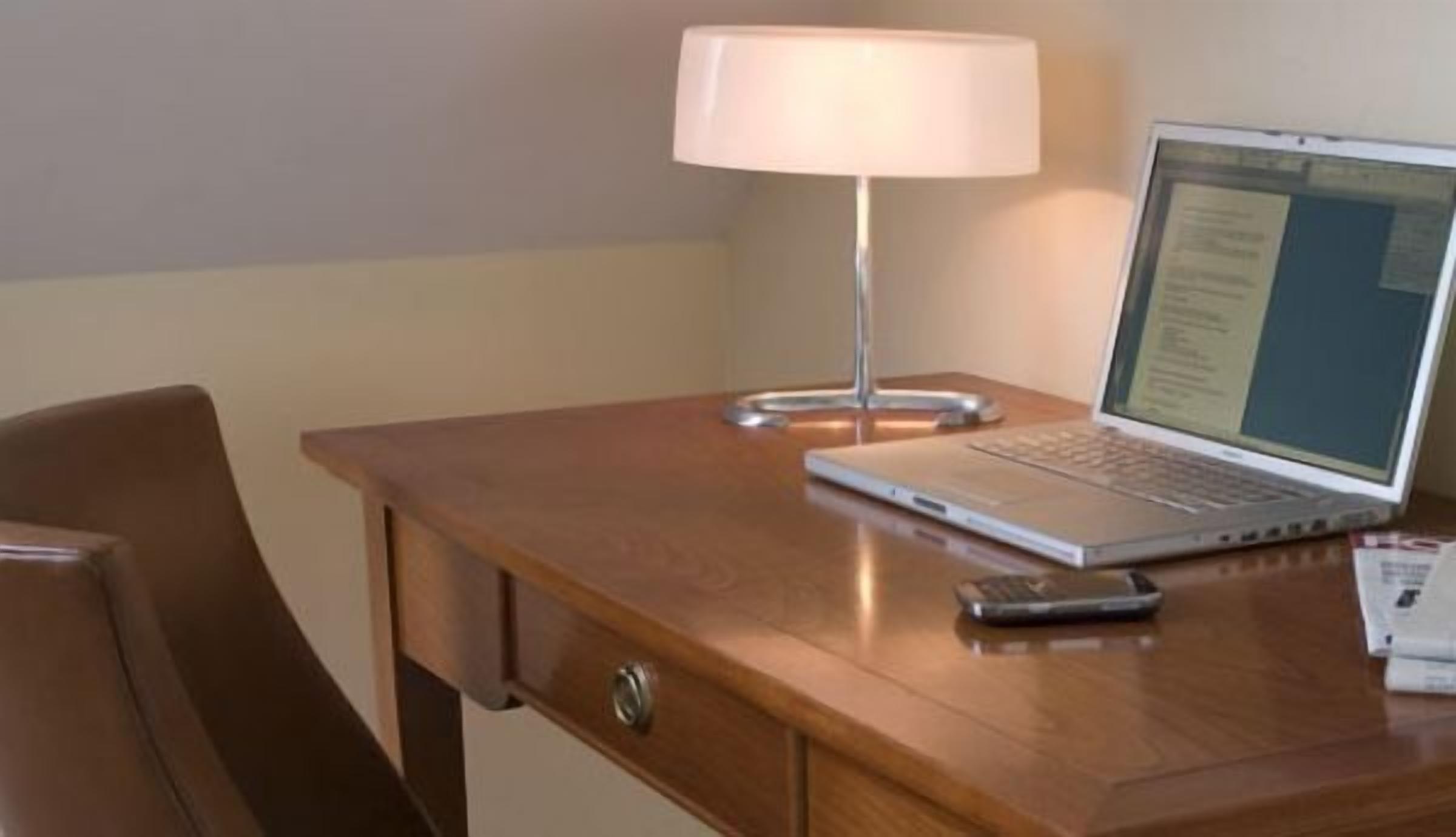 A wooden desk with a laptop, a lamp, and a remote control.