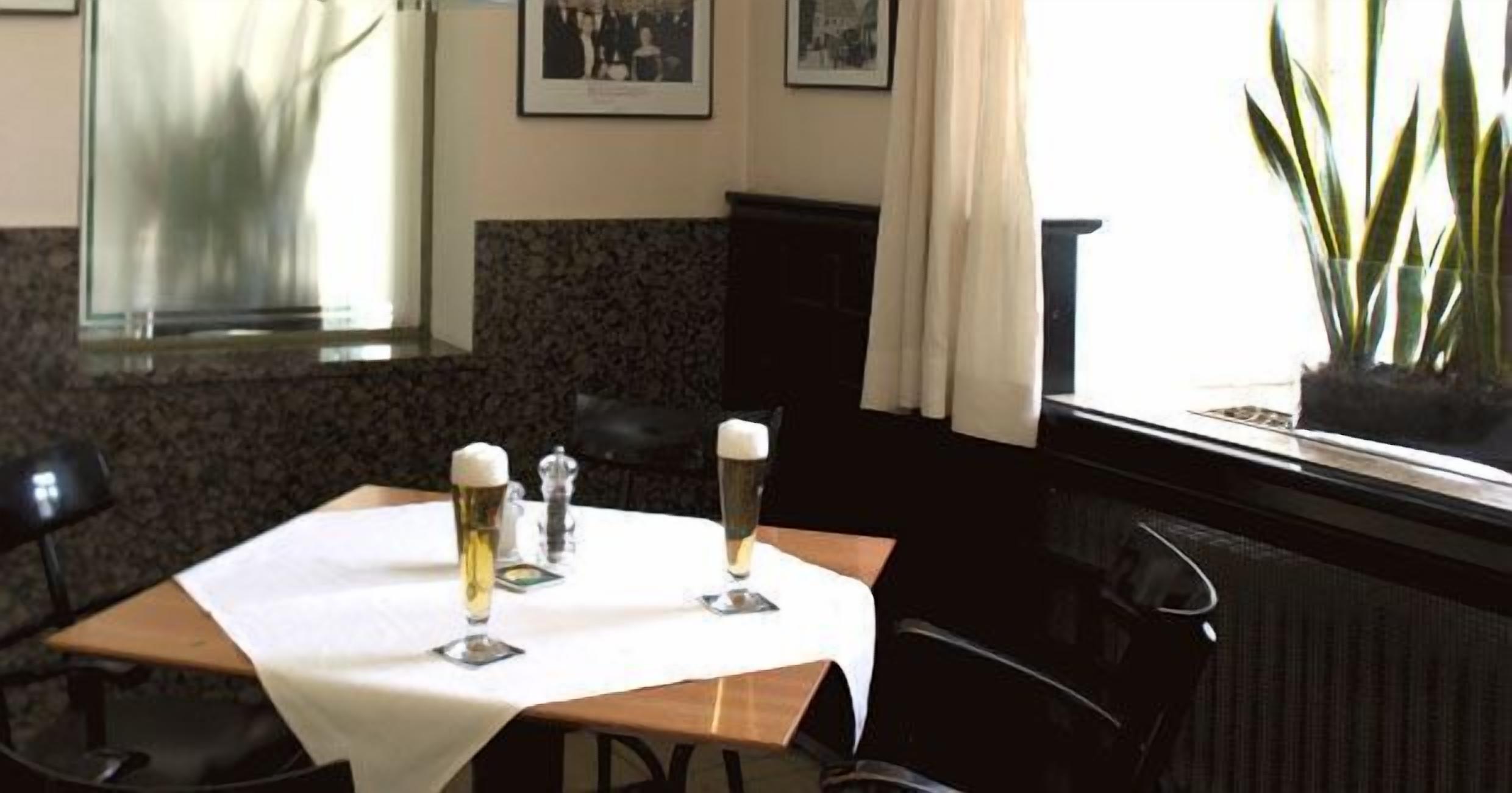 Una mesa de comedor con dos vasos de cerveza, un salero y pimentero, y un cuadro en la pared.