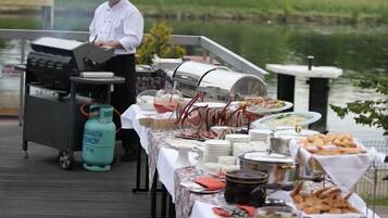 Un chef preparando comida en un muelle, con un bufé que ofrece diferentes platillos y un cilindro de gas.