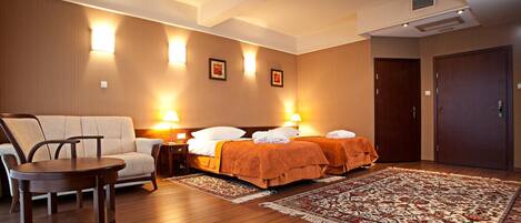 Habitación de hotel con sofá, una silla, una cama con dos almohadas, una mesita de noche y una alfombra.