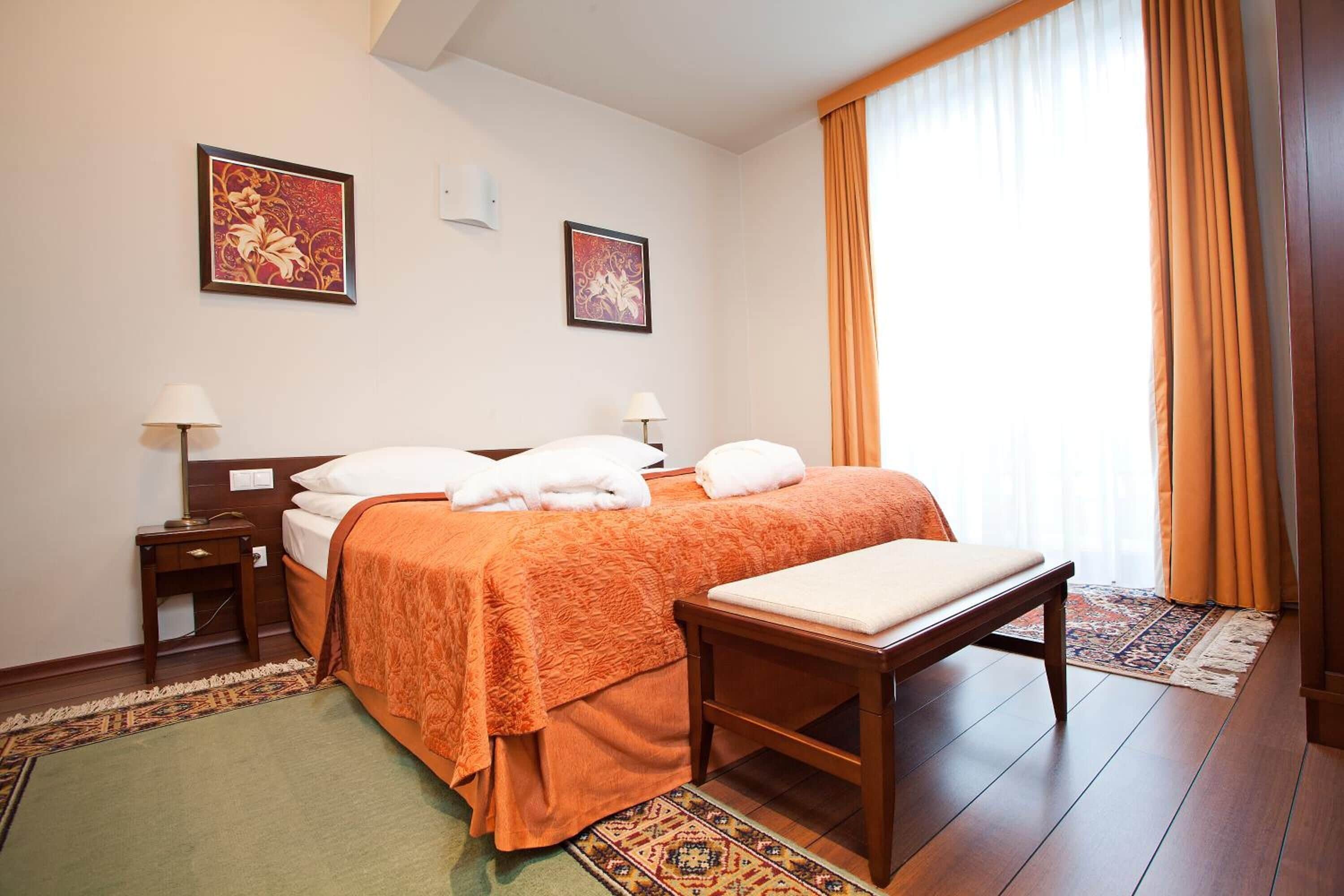 Habitación de hotel con cama, mesitas de noche, un banco y dos cuadros colgados en la pared.