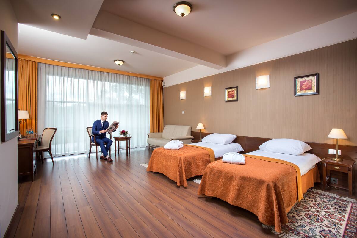 A hotel room with two beds, a desk, a chair, and a large window with curtains.