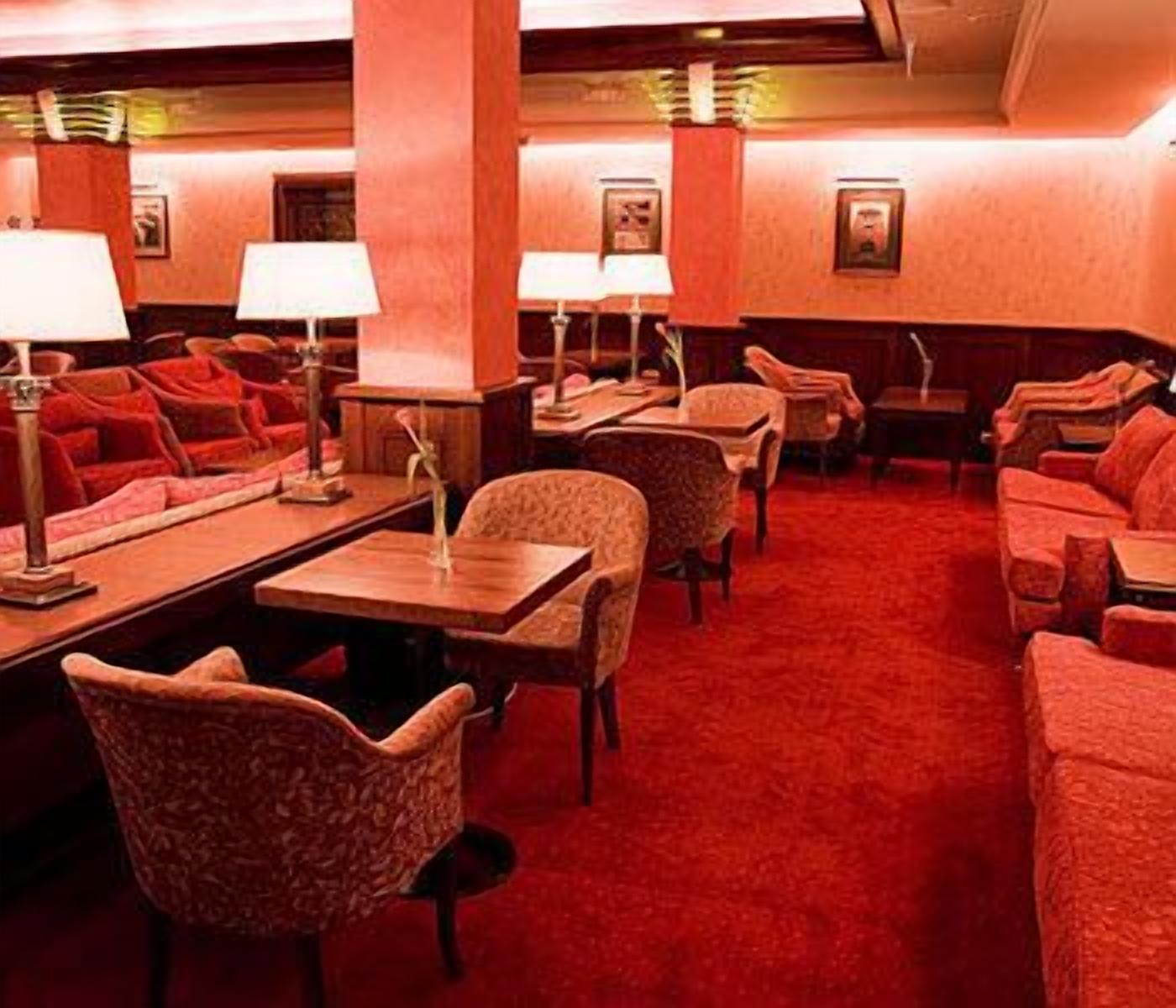 A hotel lobby with red carpet, multiple seating areas, and tables with lamps.