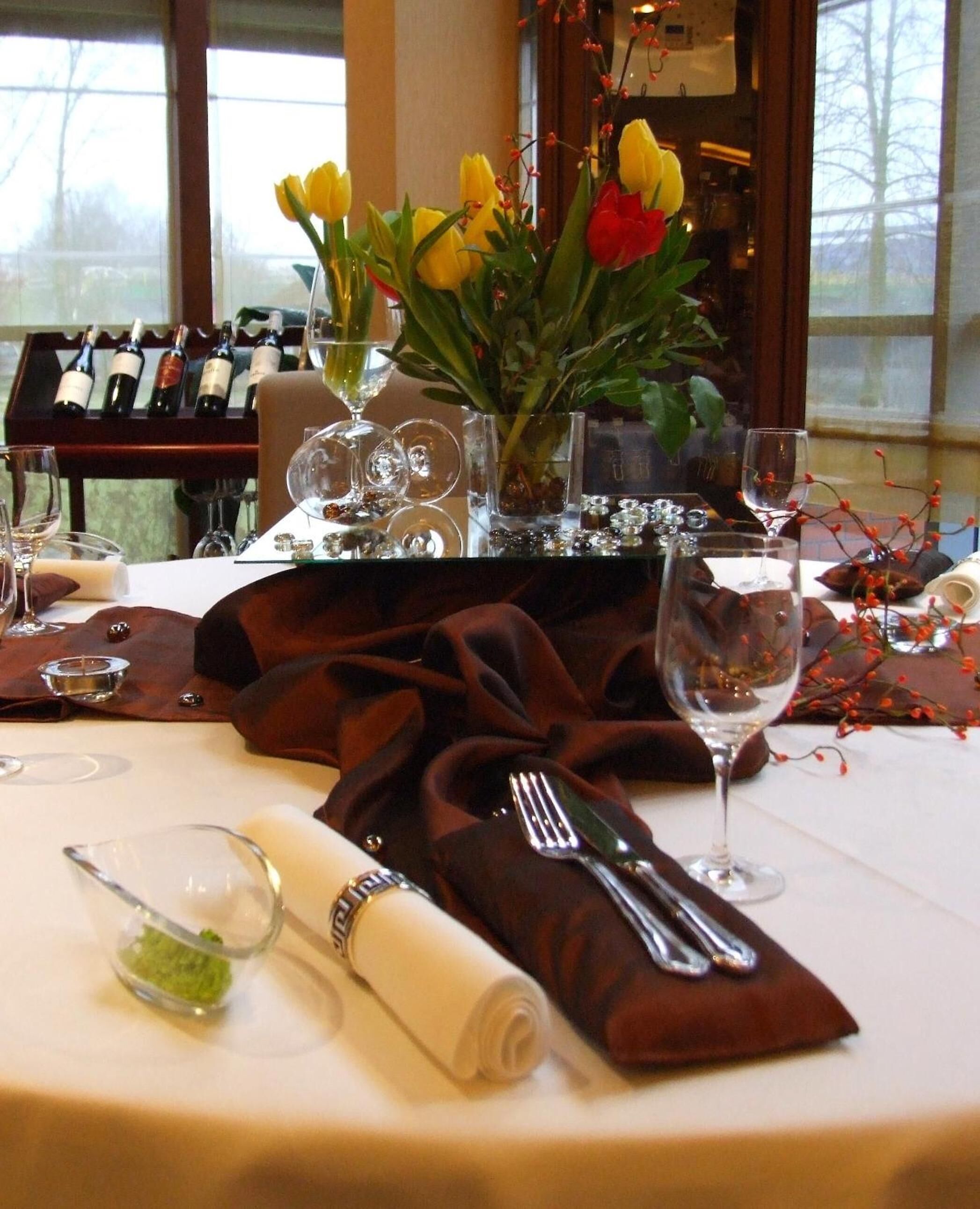 Una mesa dispuesta para una comida, con una selección de vinos, un jarrón con flores y vistas al exterior.