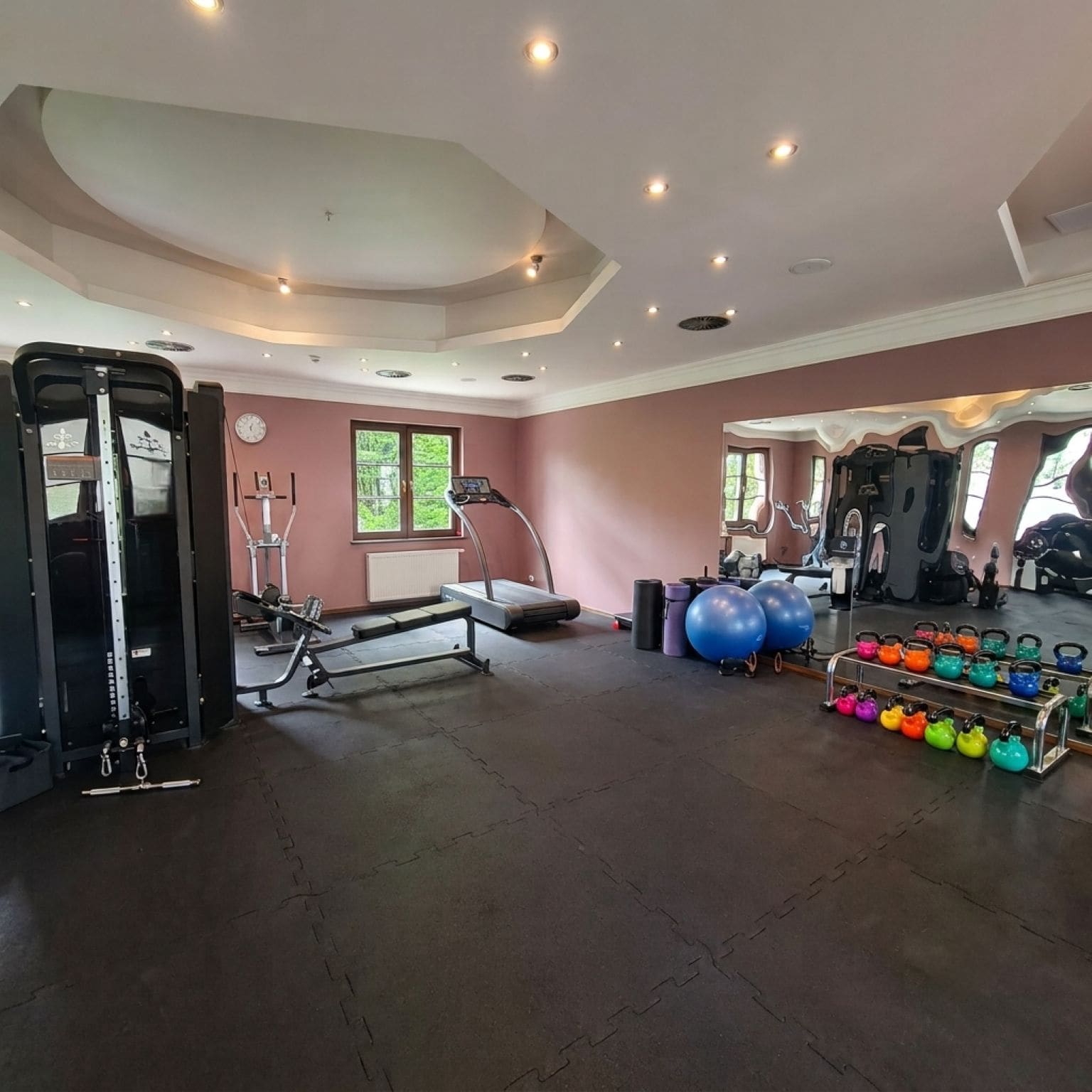 Een fitnessruimte met trainingsapparatuur, een loopband en kettlebells.
