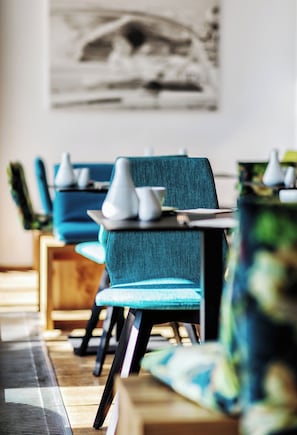 A restaurant interior with teal chairs, white table settings, and a wall-mounted painting. - Seehotel Litz (Langenargen)
