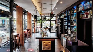 Una zona de bar con mostrador, asientos y estanterías llenas de botellas.