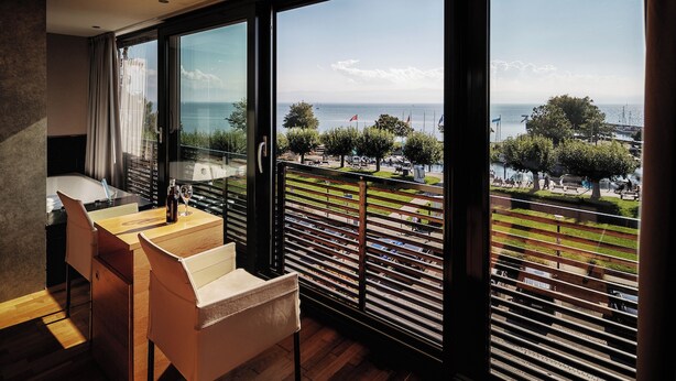 Una habitación de hotel moderna con un ventanal que ofrece vistas al mar y al paisaje urbano.