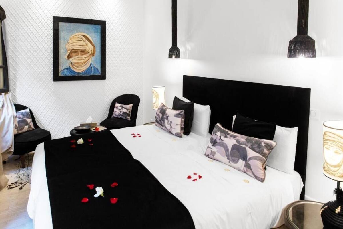 Habitación de hotel con cama, almohadas, una silla, mesita de noche, lámpara y un cuadro en la pared.
