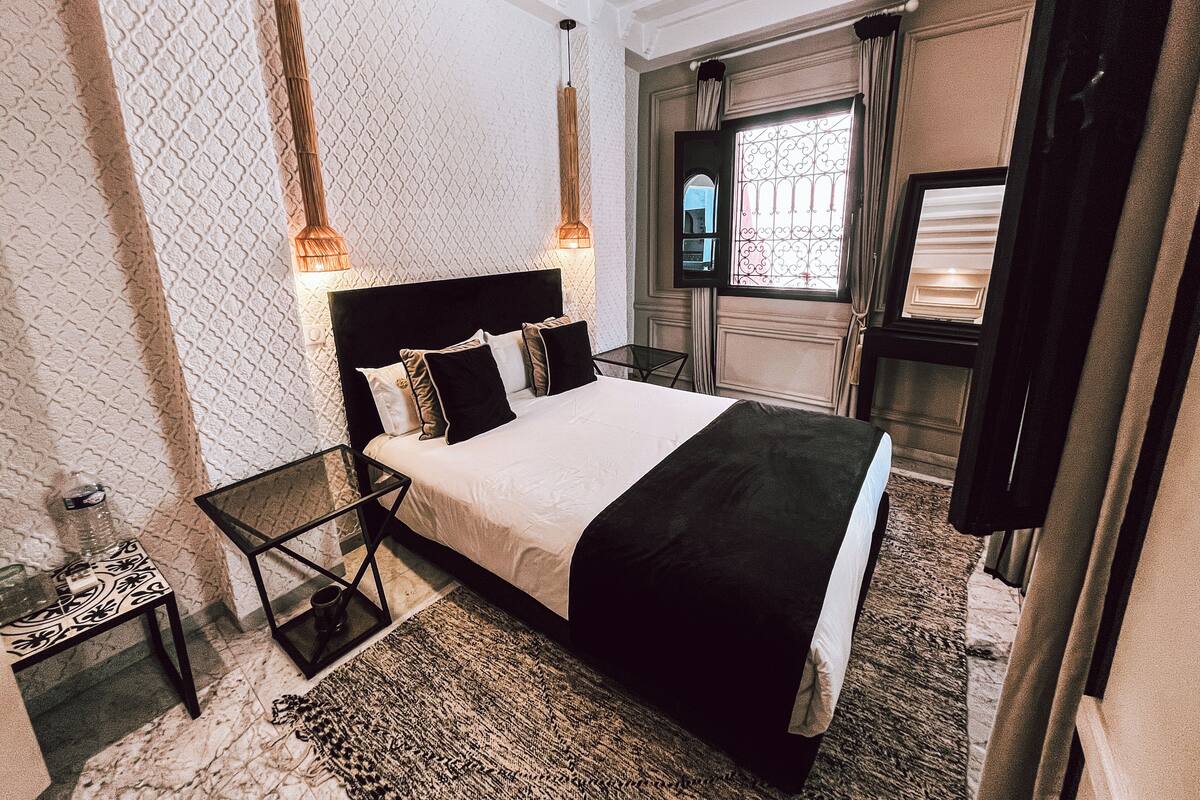 Una habitación de hotel con una cama grande, una mesita de vidrio, una mesita pequeña y un espejo.