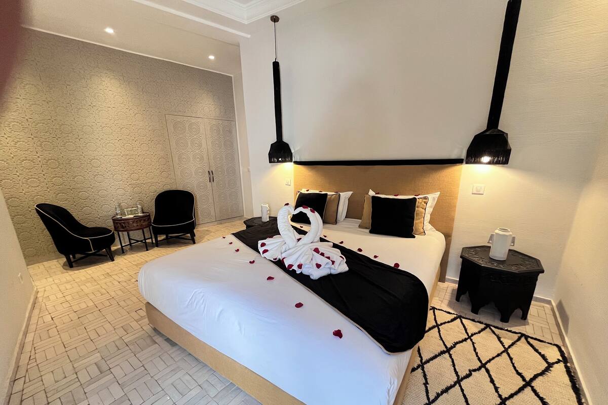 Habitación de hotel con una cama grande, una silla, una mesita pequeña y una decoración de toallas.