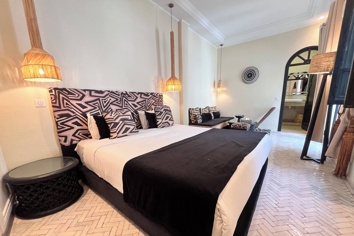 Una habitación de hotel con una cama grande, dos mesitas de noche, una silla y un espejo.