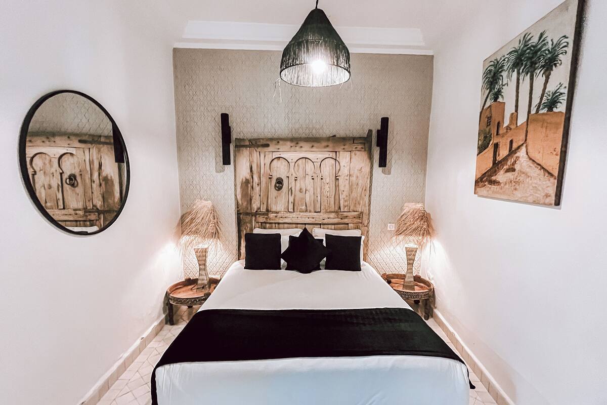 Un dormitorio con una cama, dos lámparas de noche, un candelabro colgante, un espejo y un cuadro en la pared.