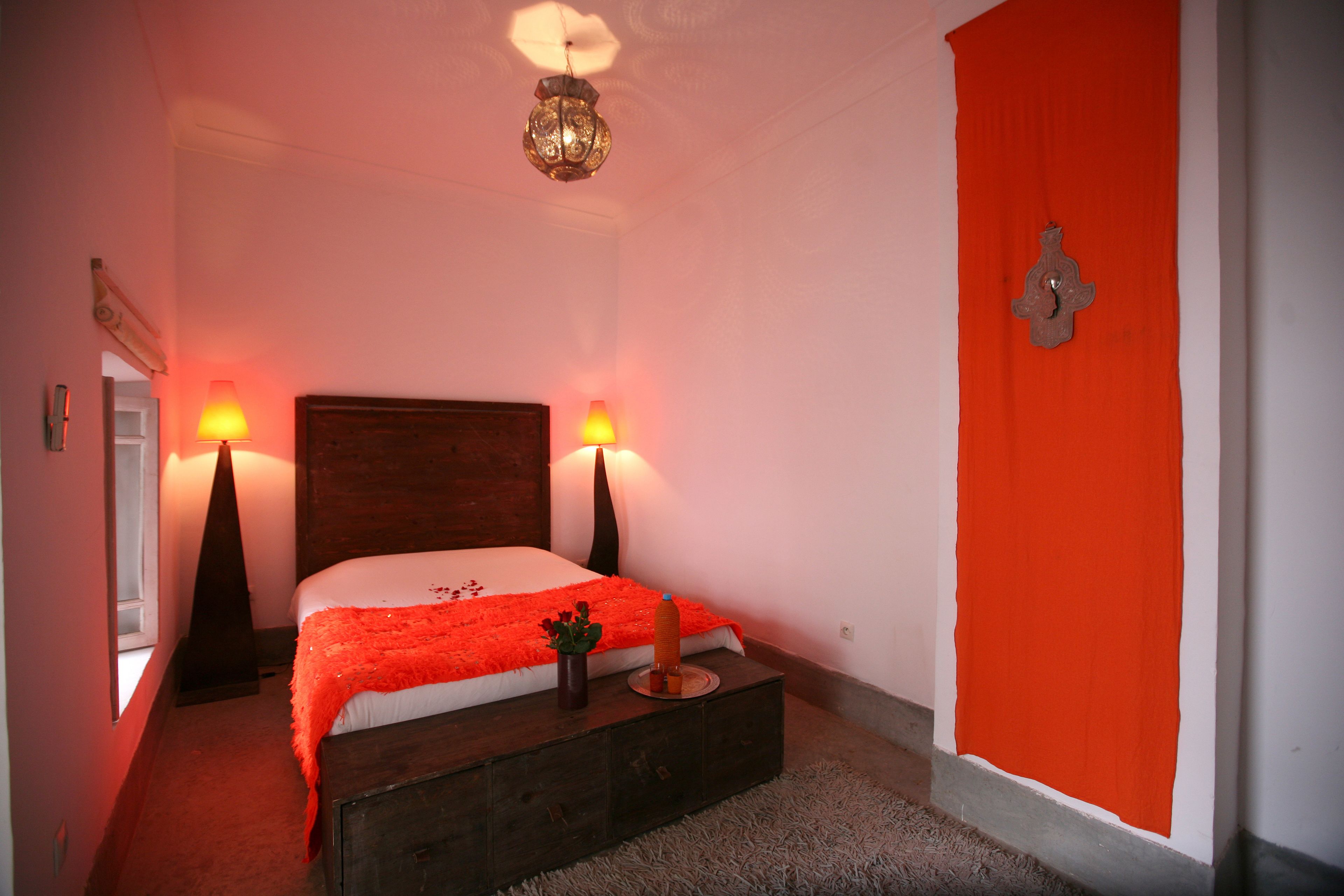 A bedroom with a wooden bed, two bedside lamps, a red accent wall, and a decorative wall piece.