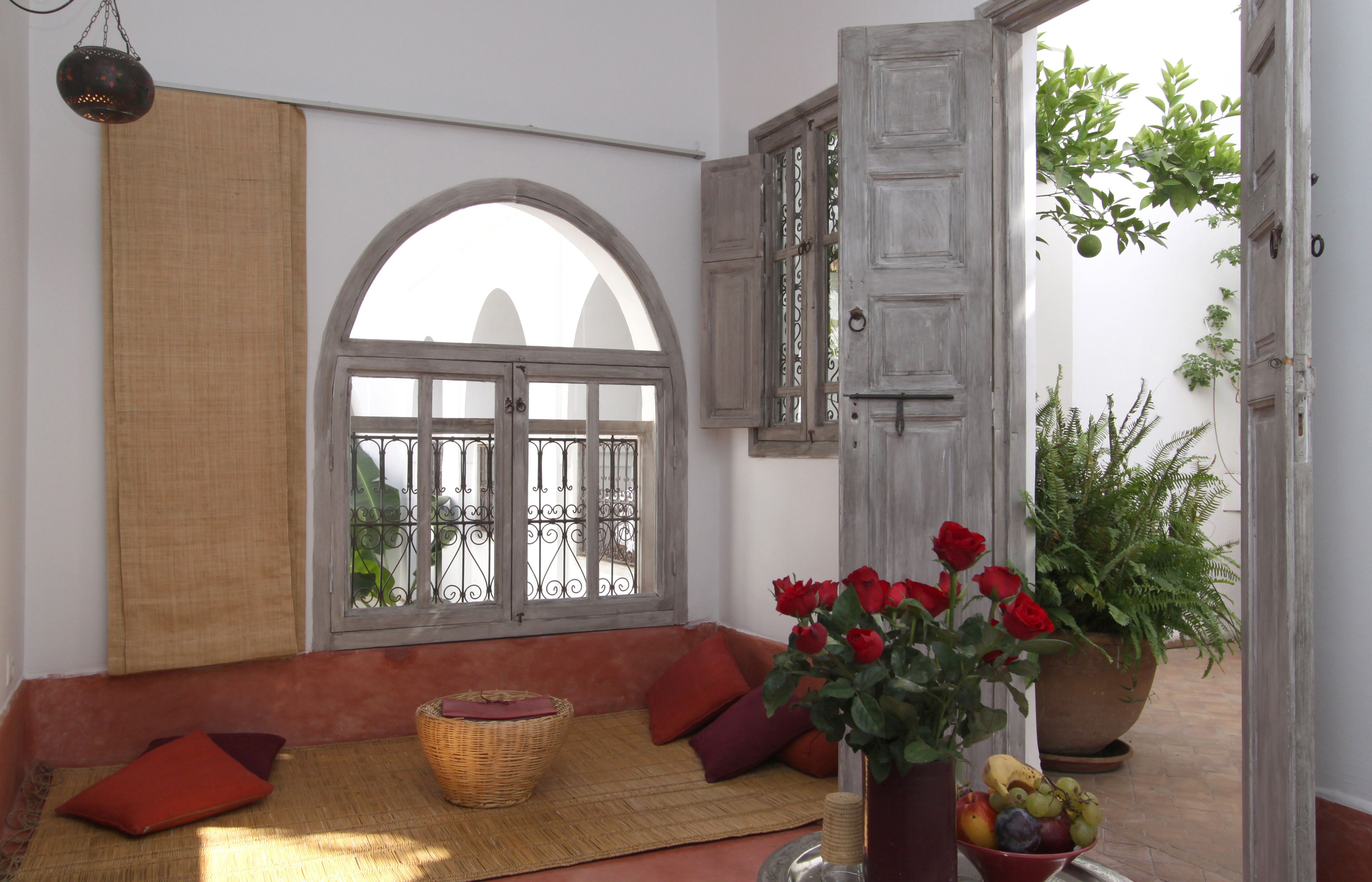A room with a large arched window, a wicker basket, a vase with red roses, and a potted plant.
