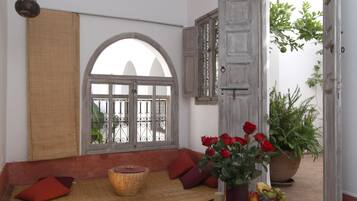 A room with a large arched window, a wicker basket, a vase with red roses, and a potted plant.