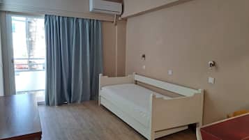 Un dormitorio con cama, una mesa de madera, un equipo de aire acondicionado y vistas a través de una ventana con cortinas.