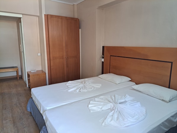 A neatly made bed with white linens and a wooden headboard, a wooden wardrobe, and a small bedside table with a remote control. - Bristol Hotel & Apartments (Kos)