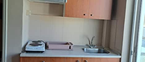 Una cocina compacta con armarios de madera, un microondas integrado y un lavabo.
