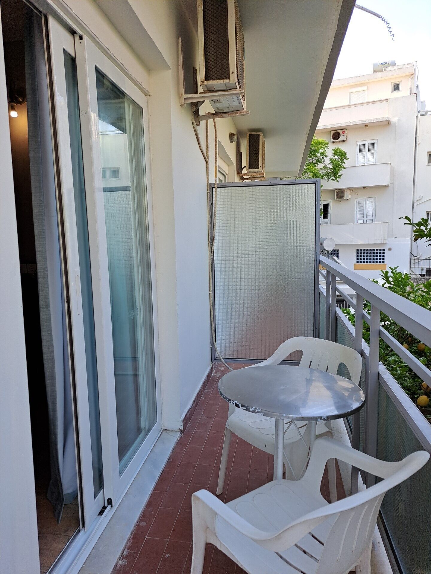 Un balcon avec une porte-fenêtre coulissante, une petite table et deux chaises en plastique blanc.