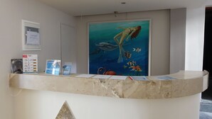 Una recepción con un cuadro de una sirena y vida marina, una puerta y carteles informativos.