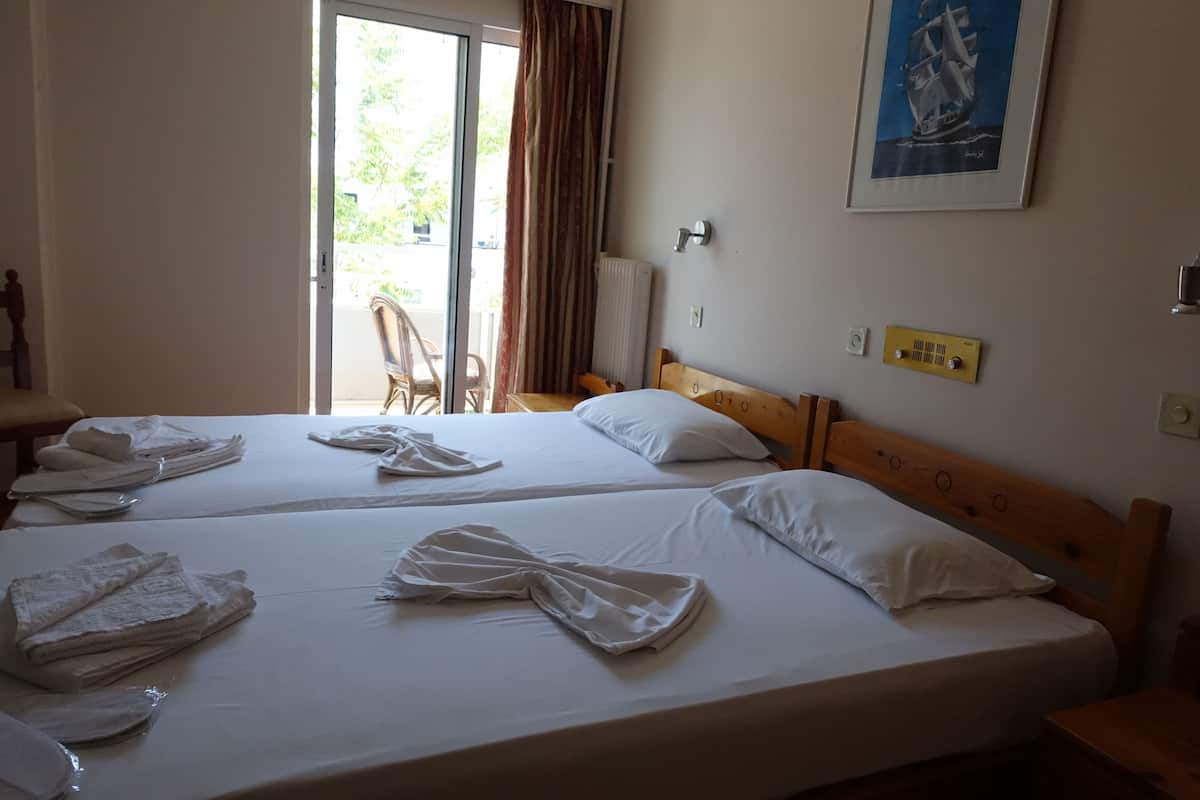 Habitación de hotel con dos camas, vista al exterior, un cuadro enmarcado en la pared y una ventana con cortinas.