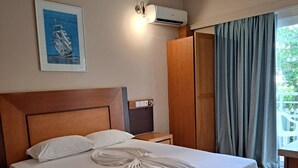 Habitación de hotel con cama de madera, mesita de noche, aire acondicionado instalado en la pared y ventana con cortinas.