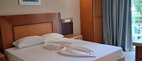 Quarto de hotel com cama de madeira, mesa de cabeceira, ar condicionado fixado na parede e janela com cortinas.