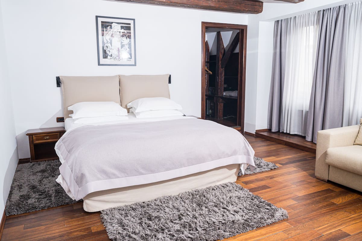 A bedroom with a bed, nightstands, a sofa, a door, and a window with curtains.