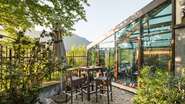 Uma área de pátio com mesa e cadeiras, cercada por vegetação e vista para as montanhas.