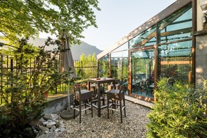 A patio area with a table and chairs, surrounded by greenery and a mountain view.