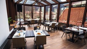 Um restaurante com várias mesas e cadeiras, grandes janelas e vista para prédios.