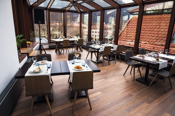 Un restaurante con varias mesas y sillas, amplias ventanas y vistas a edificios.