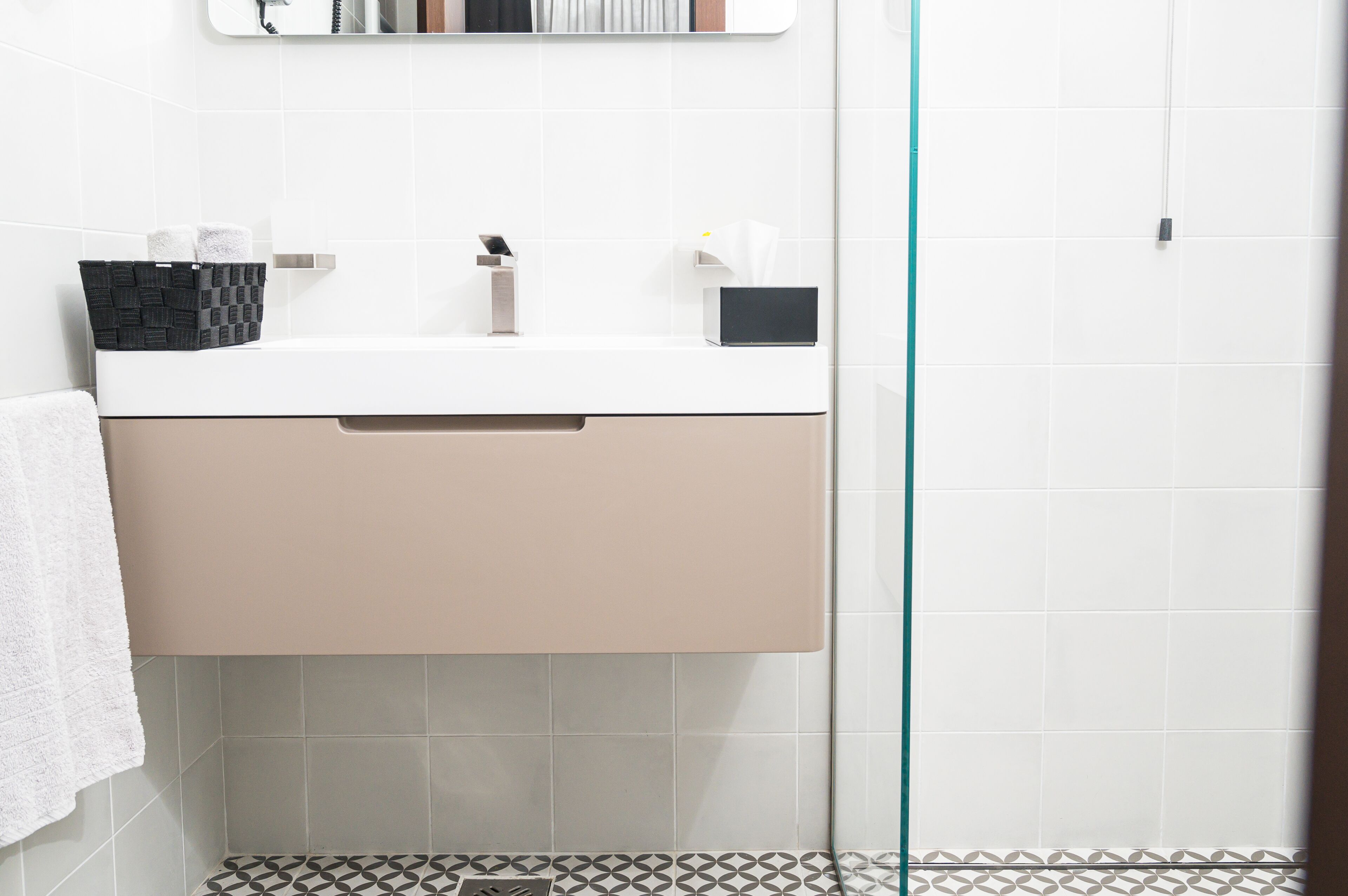 A bathroom with a white sink, beige cabinet, and patterned floor tiles.