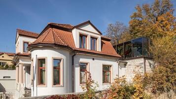 A two-story house with a red-tiled roof, a white facade, and a glass conservatory.