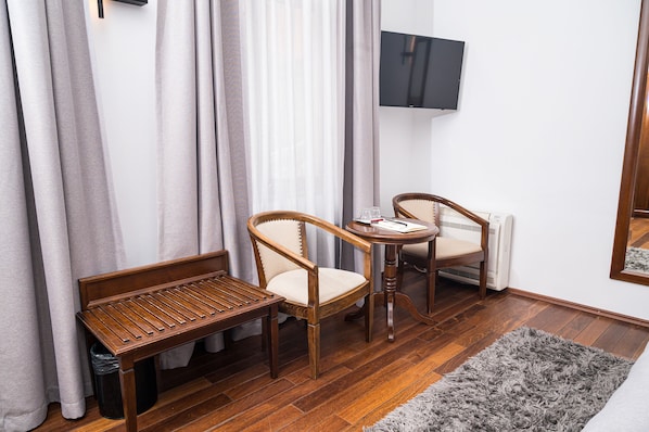 A small room with a wooden bench, two wooden chairs, a small table with a glass, and a TV mounted on the wall. - Hotel Villa Prato (Brasov)