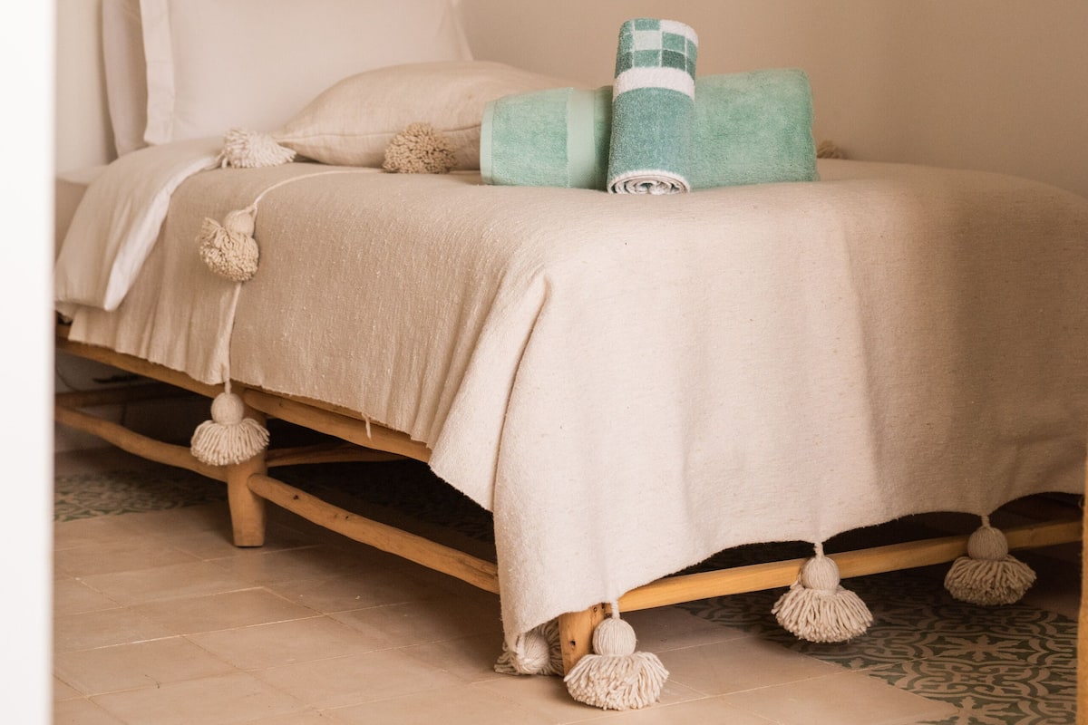 A bed with a beige bedspread, two pillows, and a teal throw blanket.