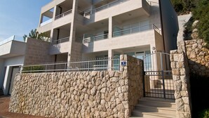 Un moderno edificio de varios pisos con balcones, un muro de piedra y un acceso con portón.