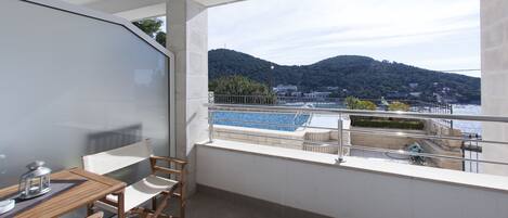 A balcony with a view of a body of water and hills, a table with chairs, and a railing.