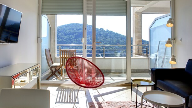Una sala de estar moderna con televisor, una butaca roja, un sofá y un balcón con vistas a una montaña.