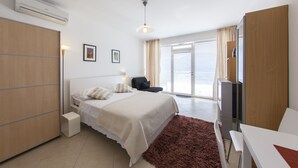 Habitación de hotel con cama, escritorio, silla, televisión y puerta corredera de vidrio al exterior.