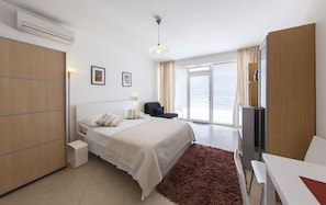 Quarto de hotel com cama, escrivaninha, cadeira, televisão e porta de correr de vidro para o exterior.
