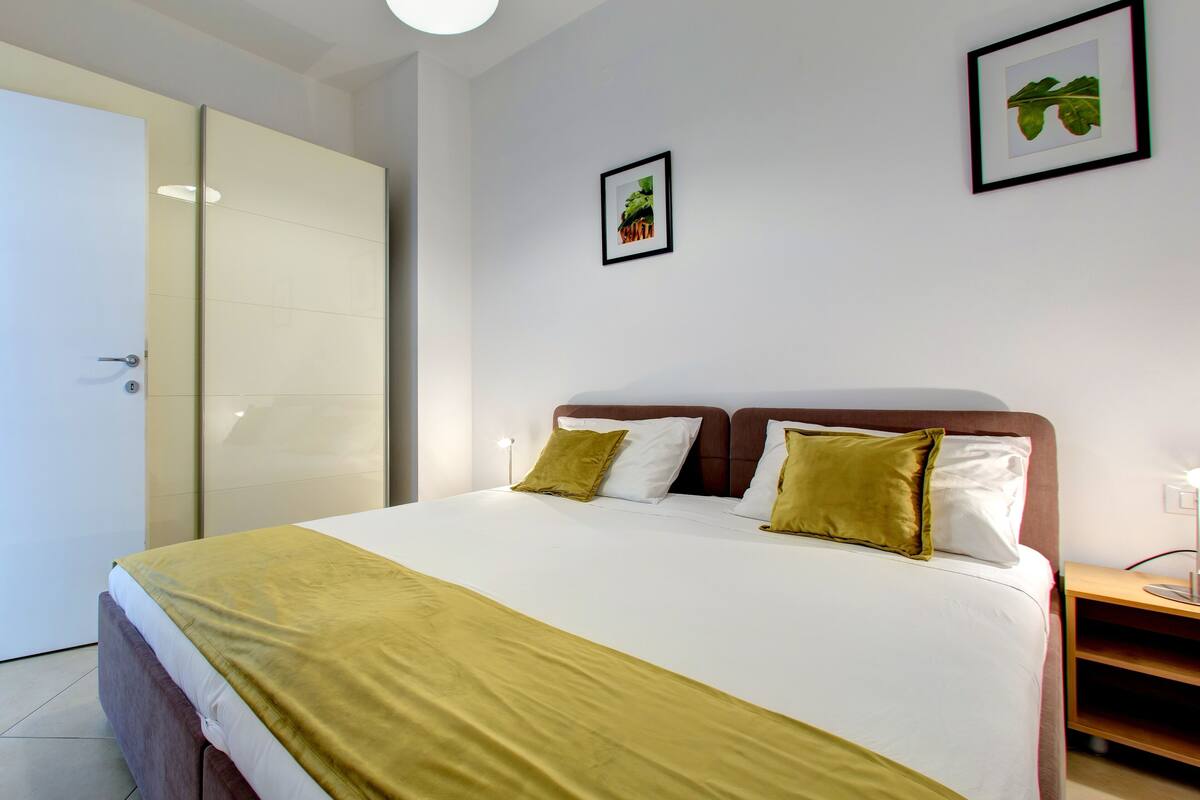 Una cama bien tendida con una colcha blanca y amarilla, dos almohadas y un cabecero de madera.