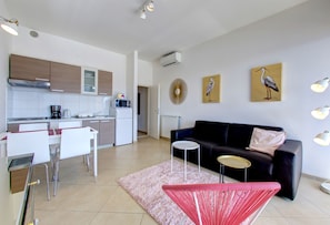 A modern living space with a kitchen, dining area, and a black sofa.