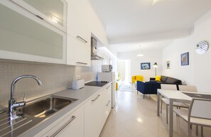 Cozinha moderna com pia de aço inoxidável, armários brancos e uma área de jantar com mesa e cadeiras.