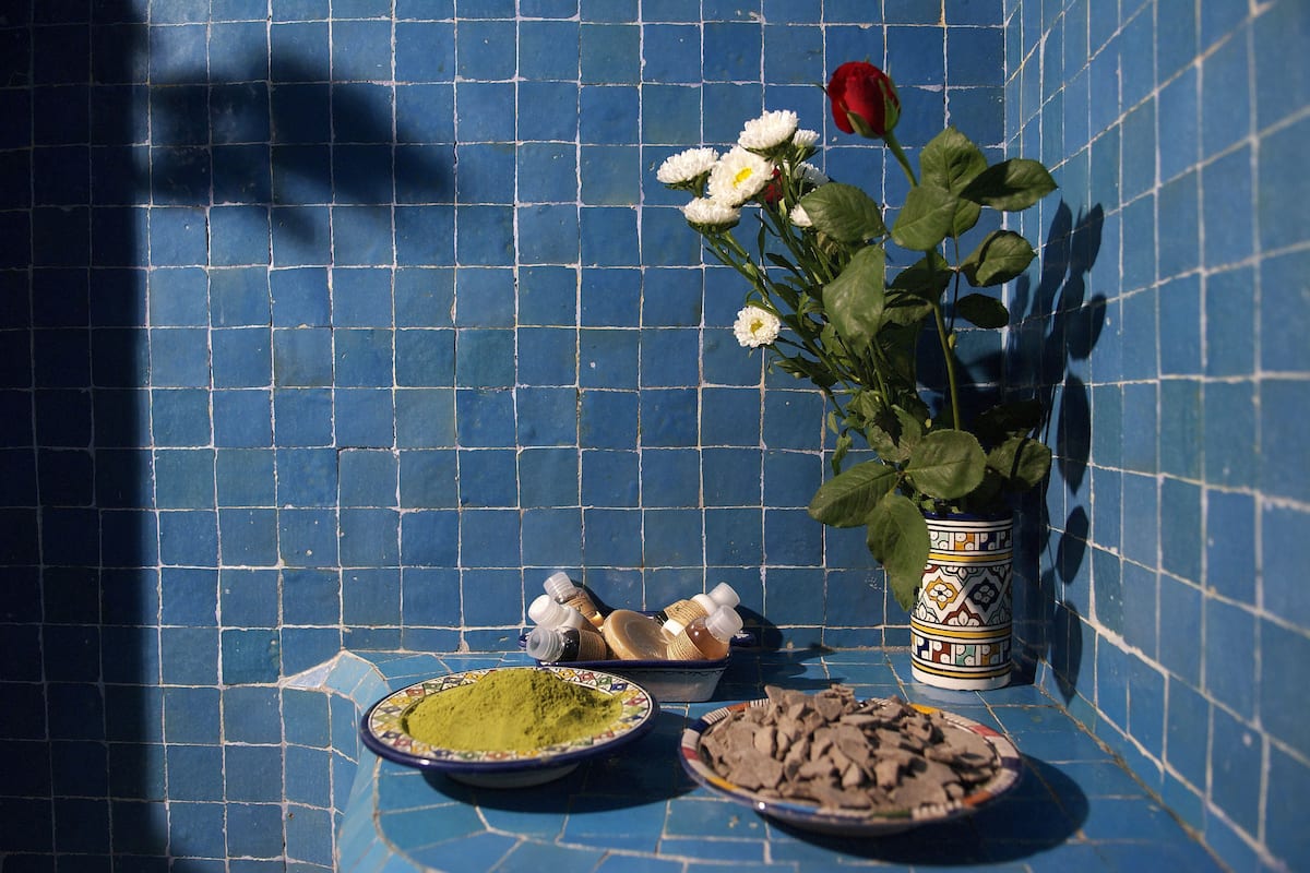 A tiled wall, a potted plant with flowers, and two bowls with powders on a table.